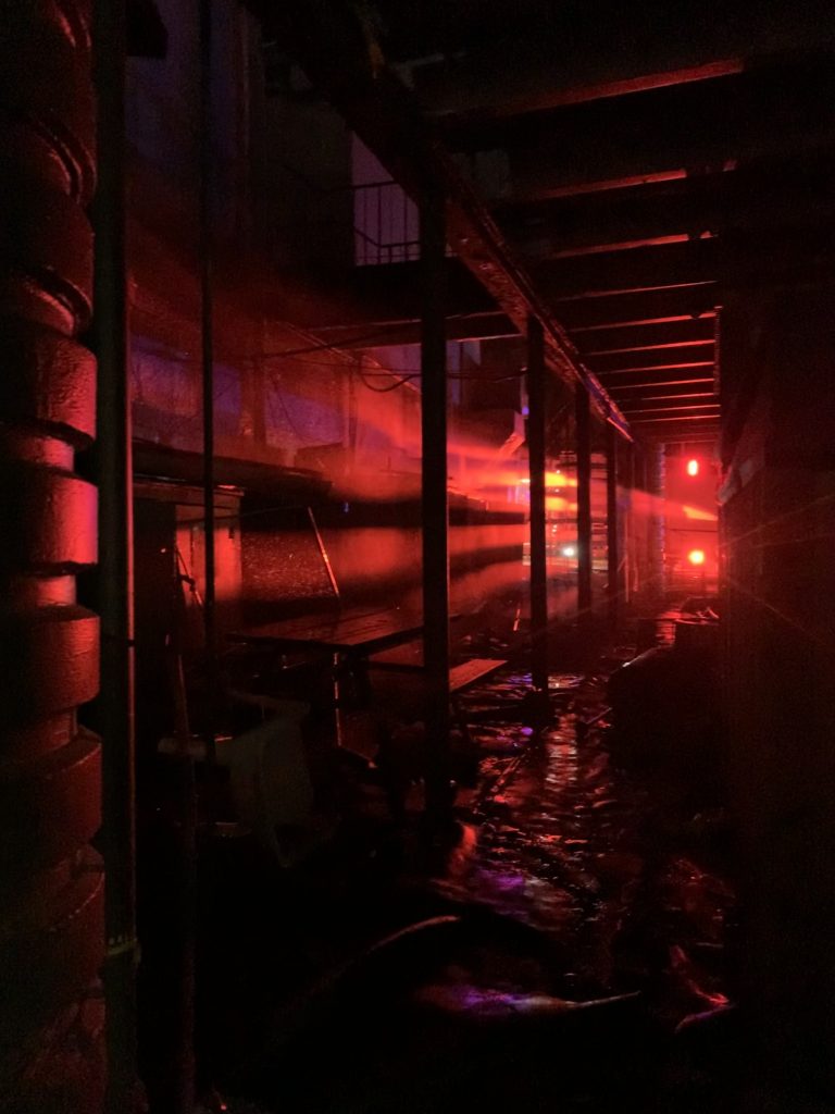 The red LED emergency lights of a fire engine are seen abstractly casting rays of light through an abandoned building.